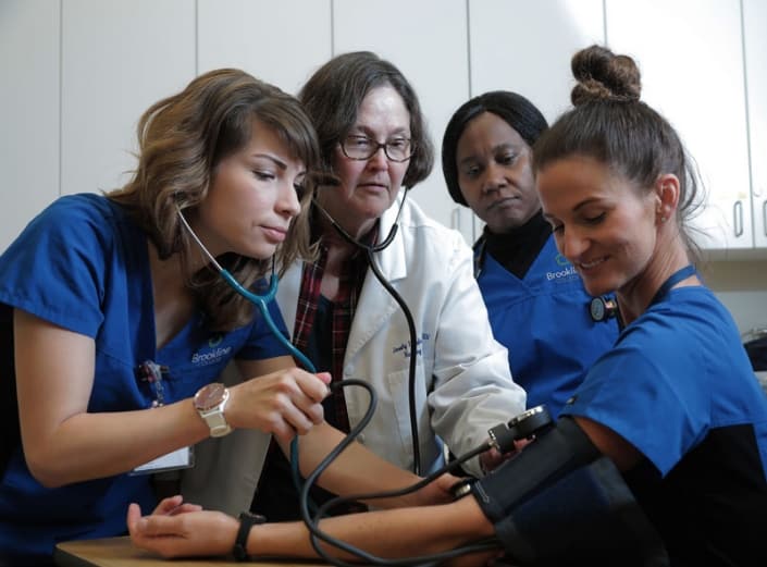 ARTY3544_logo A group of nursing students with an instructor checking the blood pressure of another student
