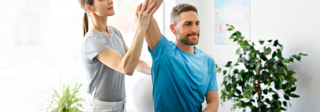 Physical therapy professional helping a man stretch his arm and shoulder
