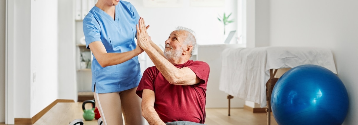 Female physical therapy professional high fiving an older patient