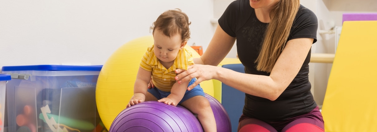 Occupational Therapy Assistant helping a small child use an exercise ball