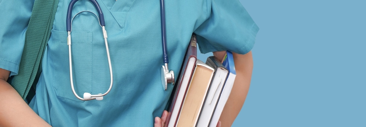 Close up of a medical student in scrubs with a stethoscope and books